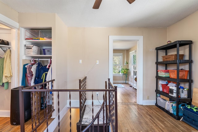 corridor with an upstairs landing, baseboards, wood-type flooring, and a textured ceiling