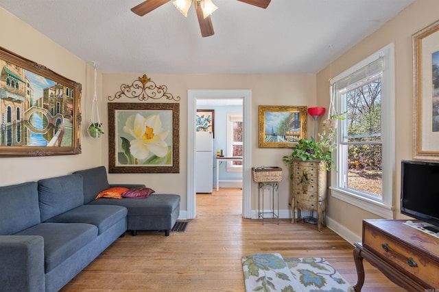 living area with visible vents, light wood-style flooring, baseboards, and ceiling fan