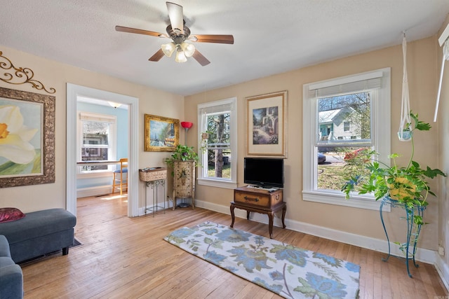 sitting room with light wood-style flooring, a textured ceiling, baseboards, and a ceiling fan