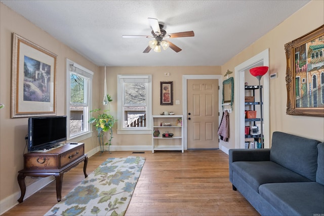 living room with visible vents, baseboards, light wood-style flooring, ceiling fan, and a textured ceiling