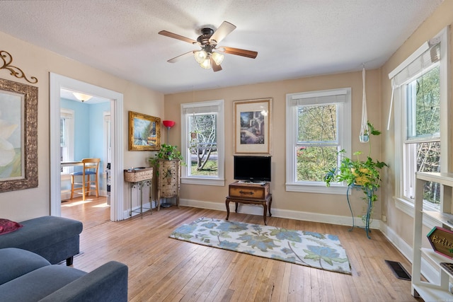 living area featuring baseboards, visible vents, light wood finished floors, ceiling fan, and a textured ceiling