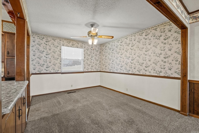 carpeted empty room with visible vents, a textured ceiling, wallpapered walls, baseboards, and ceiling fan