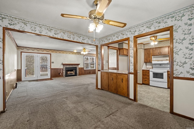 unfurnished living room featuring a wainscoted wall, light colored carpet, ceiling fan, and wallpapered walls