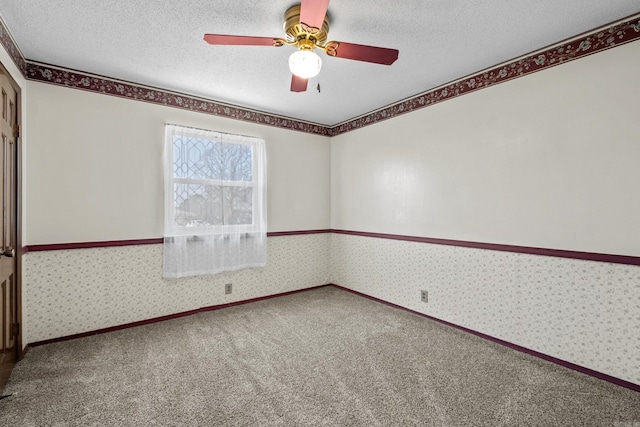 carpeted empty room featuring a ceiling fan, a textured ceiling, wainscoting, and wallpapered walls