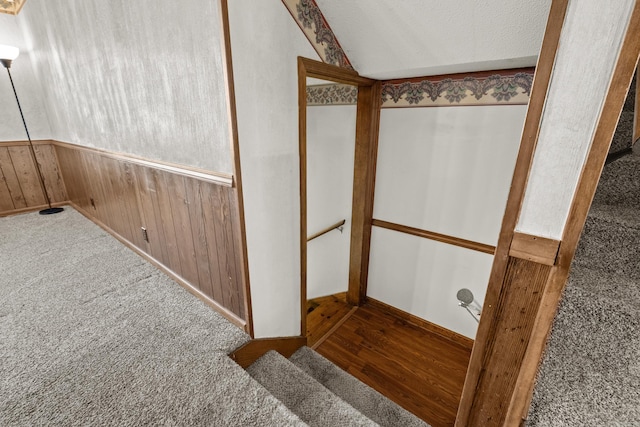 stairway with wooden walls, vaulted ceiling, carpet floors, wainscoting, and a textured ceiling