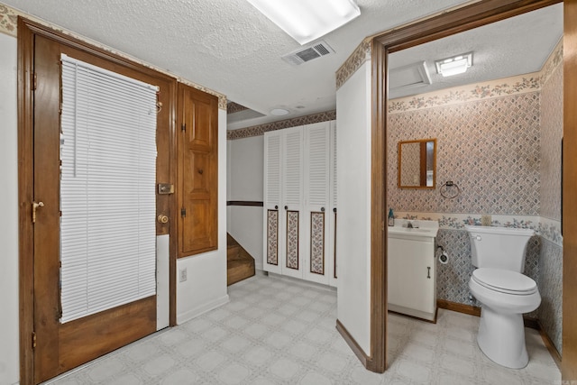 bathroom featuring wallpapered walls, tile patterned floors, visible vents, and a textured ceiling