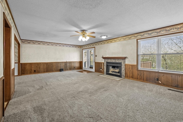 unfurnished living room with ceiling fan, a wainscoted wall, and a textured ceiling