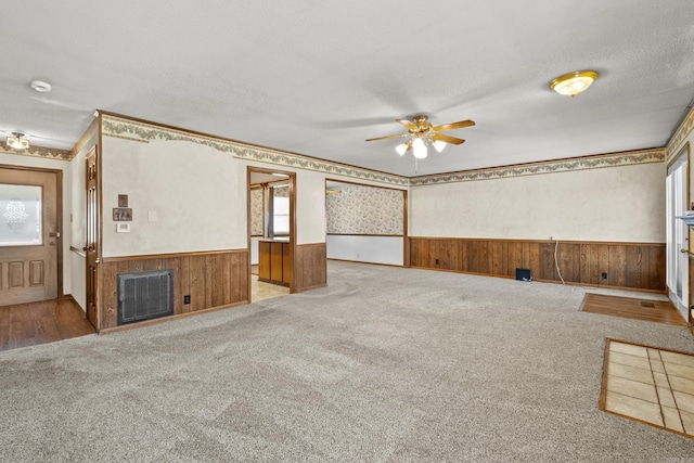 unfurnished living room with a wainscoted wall, ceiling fan, a textured ceiling, and visible vents