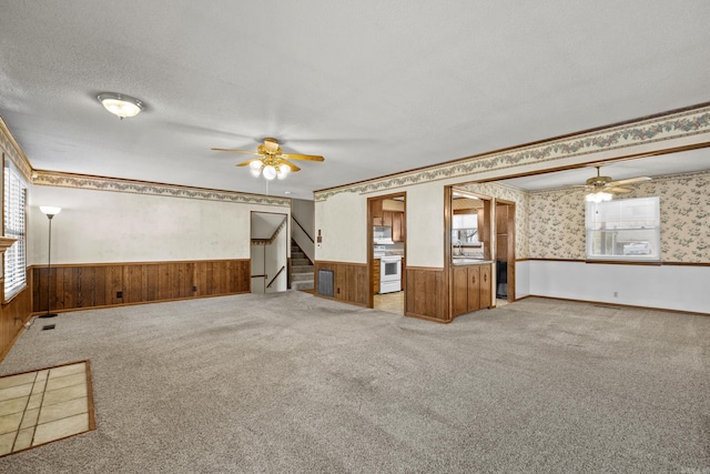 unfurnished room with ceiling fan, a textured ceiling, wallpapered walls, and wainscoting
