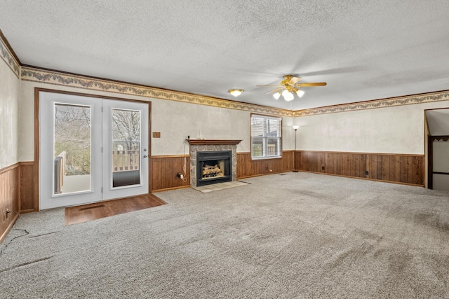 unfurnished living room featuring carpet flooring, a textured ceiling, ceiling fan, and wainscoting