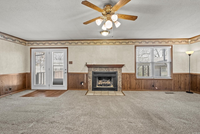 unfurnished living room with a high end fireplace, wooden walls, carpet, wainscoting, and a textured ceiling