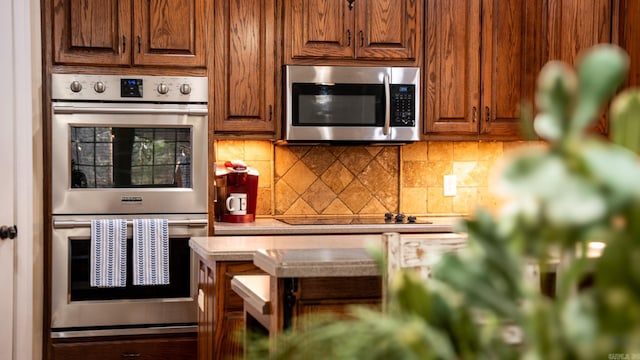 kitchen with backsplash, appliances with stainless steel finishes, brown cabinetry, and light countertops