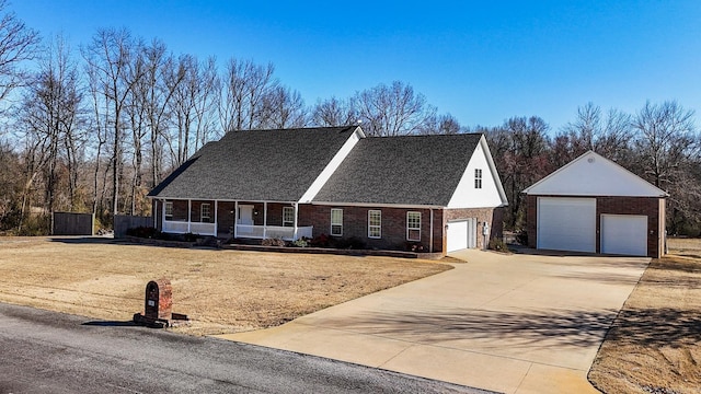 view of front of home with brick siding, covered porch, a detached garage, and an outbuilding