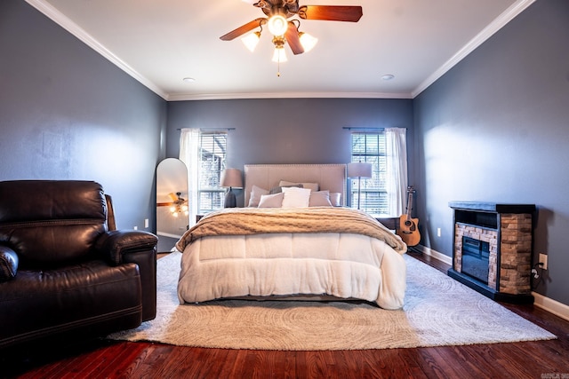 bedroom featuring a stone fireplace, ornamental molding, baseboards, and wood finished floors