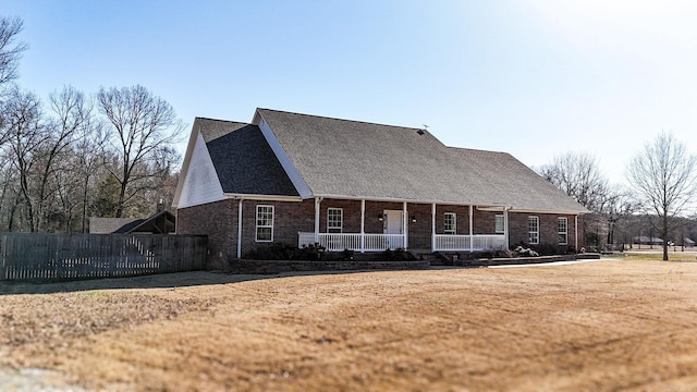 view of front of property featuring brick siding, covered porch, a front yard, and fence