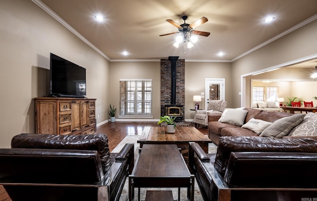 living area with baseboards, ornamental molding, a wood stove, wood finished floors, and a ceiling fan