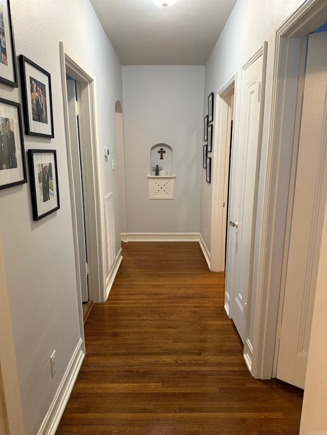 hall with baseboards, arched walkways, and dark wood-style flooring