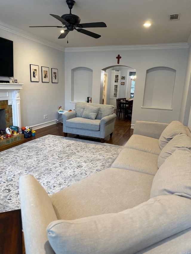 living area with visible vents, a ceiling fan, wood finished floors, arched walkways, and crown molding