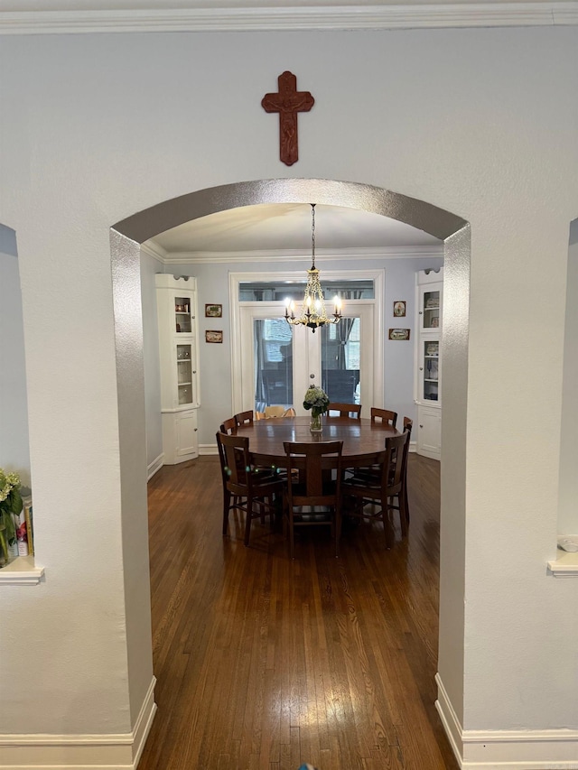 dining space with arched walkways, a notable chandelier, dark wood-type flooring, and ornamental molding