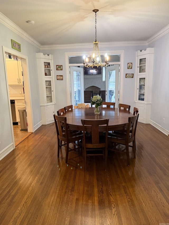 dining area featuring dark wood-type flooring, an inviting chandelier, a fireplace, crown molding, and baseboards