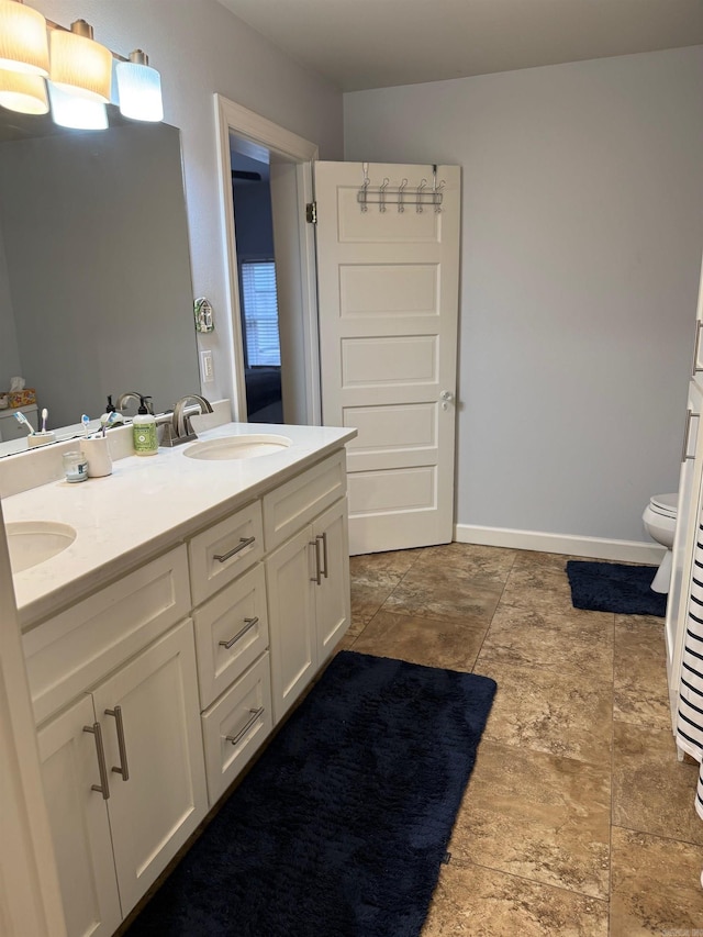 full bath with a sink, baseboards, toilet, and double vanity