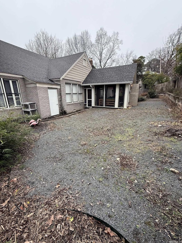 view of front of home with brick siding, fence, roof with shingles, a chimney, and a sunroom