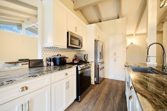 kitchen with lofted ceiling with beams, decorative backsplash, dark stone countertops, appliances with stainless steel finishes, and white cabinetry