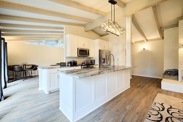 kitchen featuring light wood finished floors, vaulted ceiling with beams, a center island with sink, and stainless steel appliances