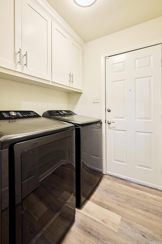 clothes washing area with cabinet space, light wood-style flooring, and separate washer and dryer