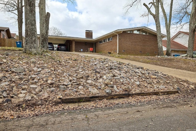 view of side of home with a carport, crawl space, brick siding, and a chimney