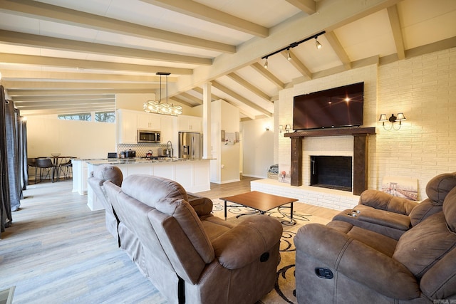 living room featuring visible vents, lofted ceiling with beams, light wood finished floors, a brick fireplace, and a chandelier