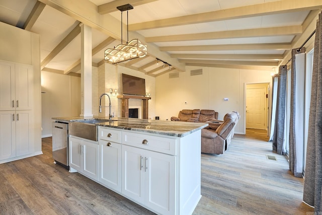 kitchen featuring light stone counters, vaulted ceiling with beams, a sink, stainless steel dishwasher, and open floor plan