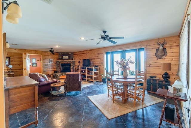 dining area featuring a stone fireplace, ceiling fan, and wood walls