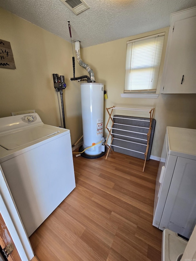 washroom with baseboards, visible vents, water heater, light wood-style floors, and a textured ceiling