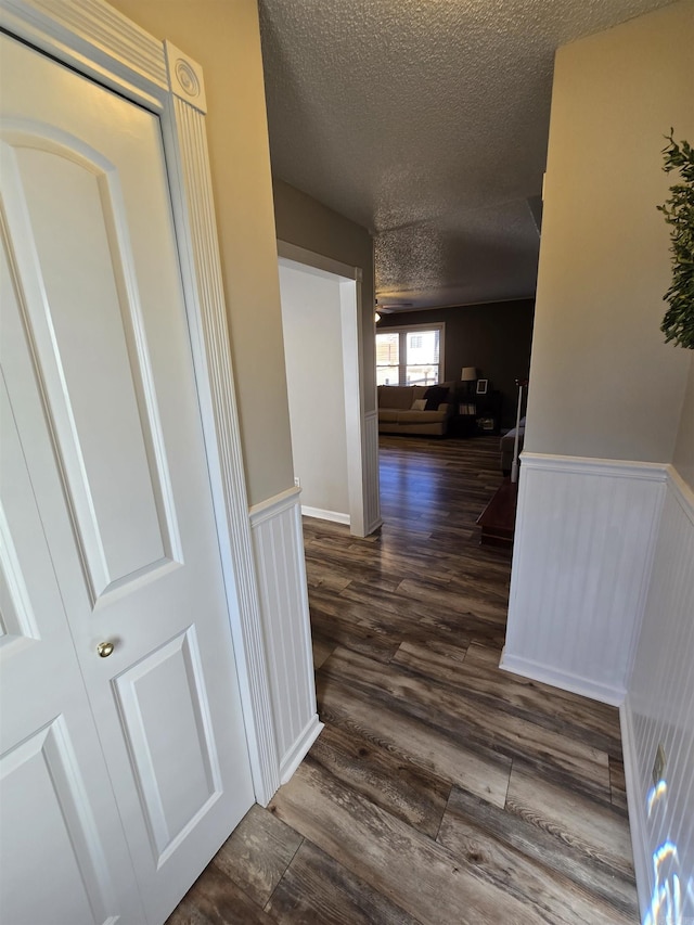 hallway with a textured ceiling, dark wood-style flooring, and wainscoting