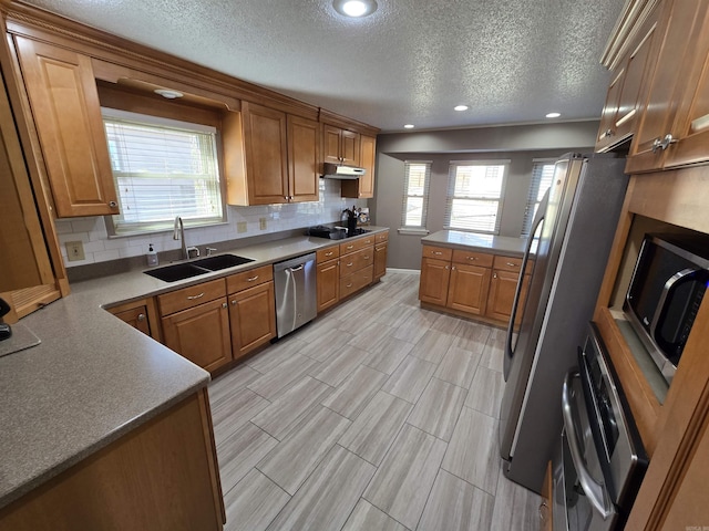 kitchen featuring a sink, decorative backsplash, under cabinet range hood, appliances with stainless steel finishes, and brown cabinets