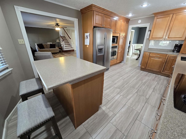 kitchen with backsplash, stainless steel appliances, light countertops, and a ceiling fan