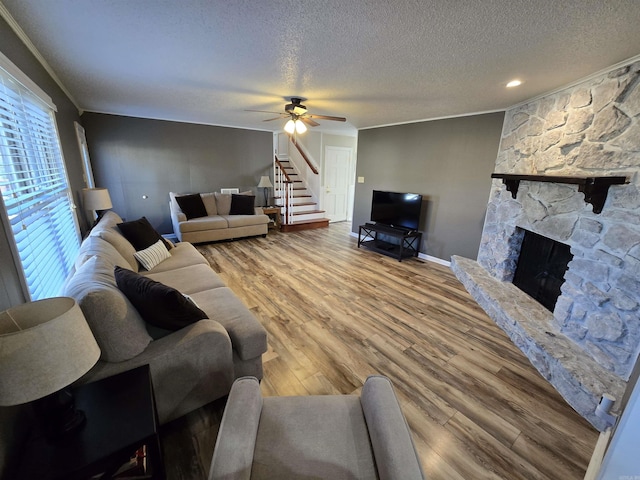 living area with ornamental molding, wood finished floors, stairway, a fireplace, and ceiling fan