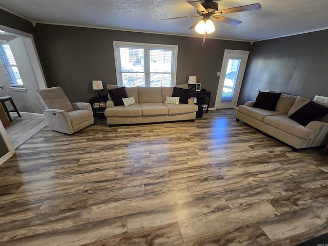 living room with ornamental molding, a ceiling fan, a textured ceiling, baseboards, and dark wood-style flooring