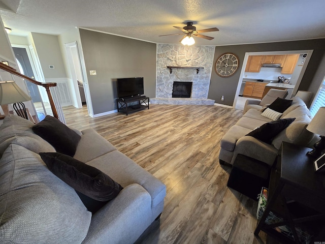 living area with a ceiling fan, baseboards, a stone fireplace, light wood-style floors, and a textured ceiling