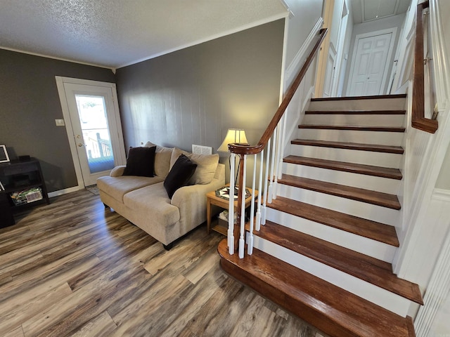 living room with ornamental molding, a textured ceiling, wood finished floors, attic access, and stairs