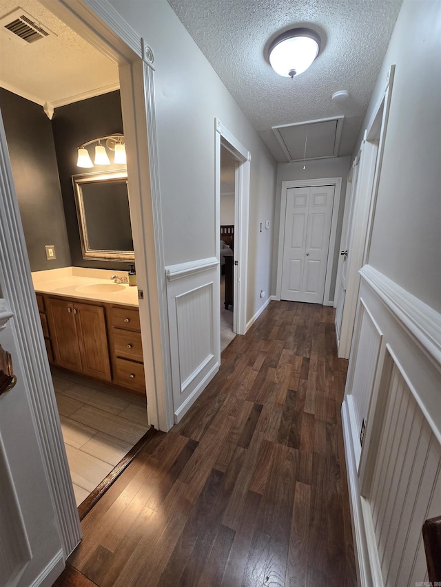 hallway with visible vents, attic access, a sink, dark wood-type flooring, and a textured ceiling