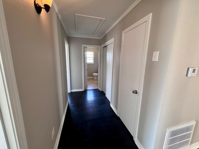 corridor with dark wood-style floors, visible vents, baseboards, attic access, and crown molding