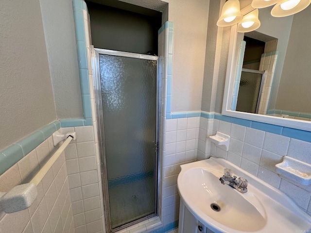 bathroom featuring a sink, tile walls, a stall shower, and wainscoting