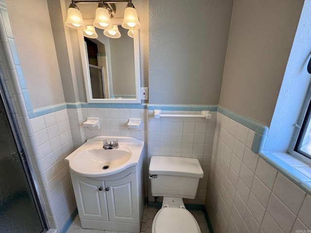 full bathroom featuring a wainscoted wall, toilet, vanity, a stall shower, and tile walls