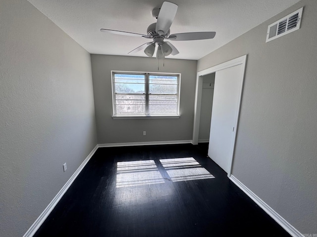 unfurnished bedroom featuring a ceiling fan, baseboards, visible vents, dark wood-type flooring, and a closet