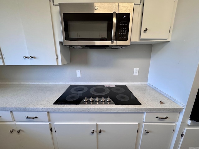 kitchen featuring stainless steel microwave, white cabinetry, light countertops, and black electric cooktop