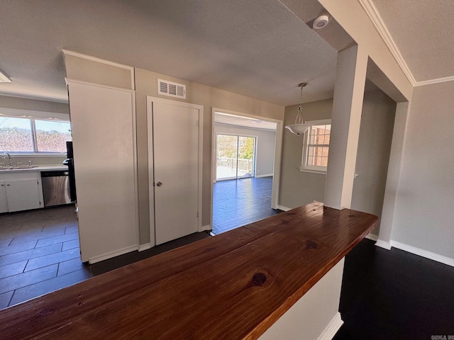 hallway with visible vents, a textured ceiling, baseboards, and a sink