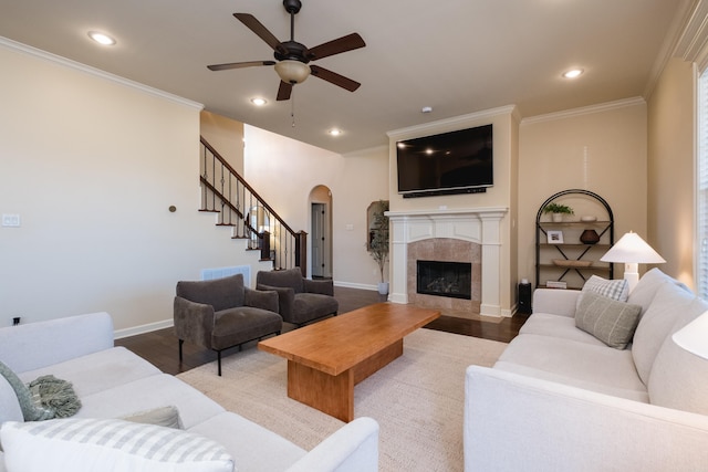 living room featuring ornamental molding, a fireplace, wood finished floors, arched walkways, and a ceiling fan