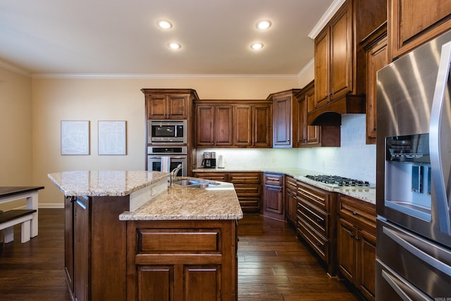 kitchen featuring a kitchen island with sink, a sink, dark wood finished floors, appliances with stainless steel finishes, and crown molding